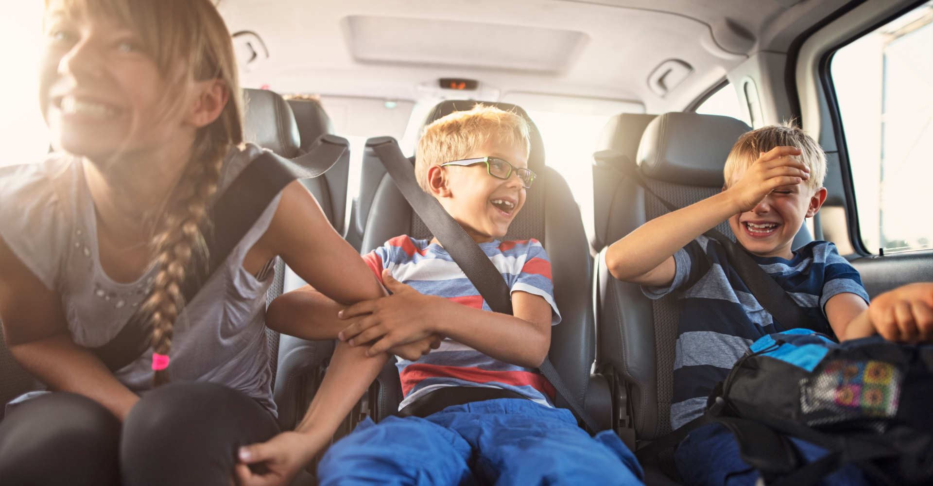 Three older children smiling and laughing in the back of a car 